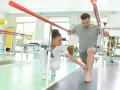Mann übt nach Physiotherapie unter Anleitung einer Therapeutin auf einer Matte.