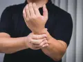Mann hält schmerzend Handgelenk, deutet auf chronische Tendinopathie.