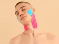 Mann mit geschlossenen Augen, dessen Kiefergelenk und Hals mit pinken und blauen Kinesio-Tapes versorgt sind.
