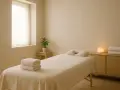 Ein heller Raum mit einer Massageliege, Handtüchern und einer kleinen Pflanze. Perfekt für eine entspannende Massage Auszeit.