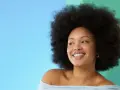 Lächelnde Frau mit Afro-Frisur vor blau-grünem Hintergrund.