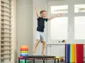 Fröhlicher Junge springt auf Trampolin, Teil der kinder physiotherapie. Kletterwand und bunte Matten im Hintergrund.