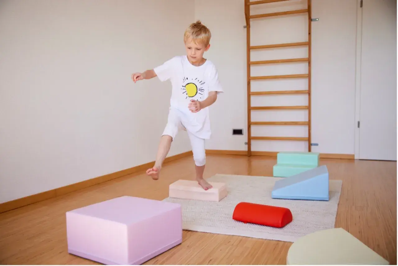 Junge übt Balancieren auf bunten Blöcken. Ergotherapie fördert die Frustrationstoleranz bei Kindern.
