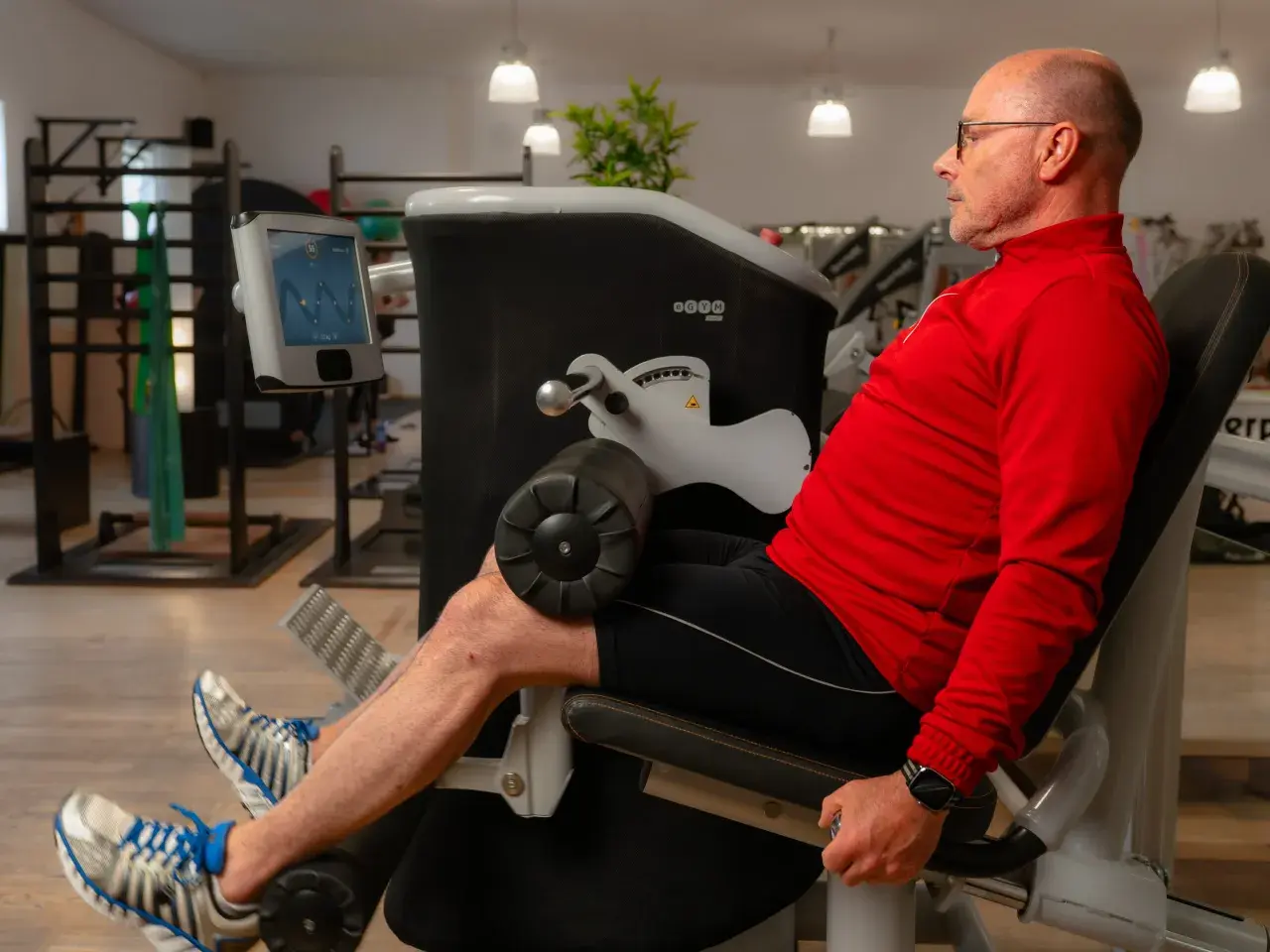 Mann trainiert Beine an einem Gerät, unterstützt von **private Physiotherapeuten** für optimale Ergebnisse.