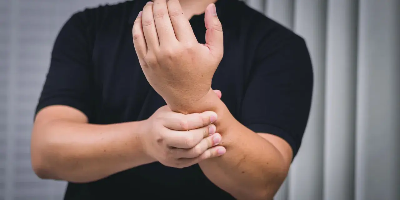 Mann hält schmerzend Handgelenk, deutet auf chronische Tendinopathie.