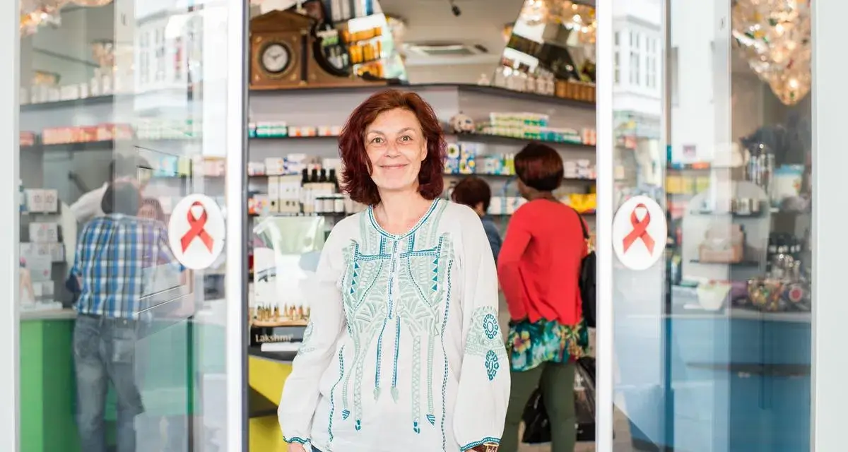 Frau lächelt vor einer Apotheke mit roten Aids-Schleifen am Eingang.