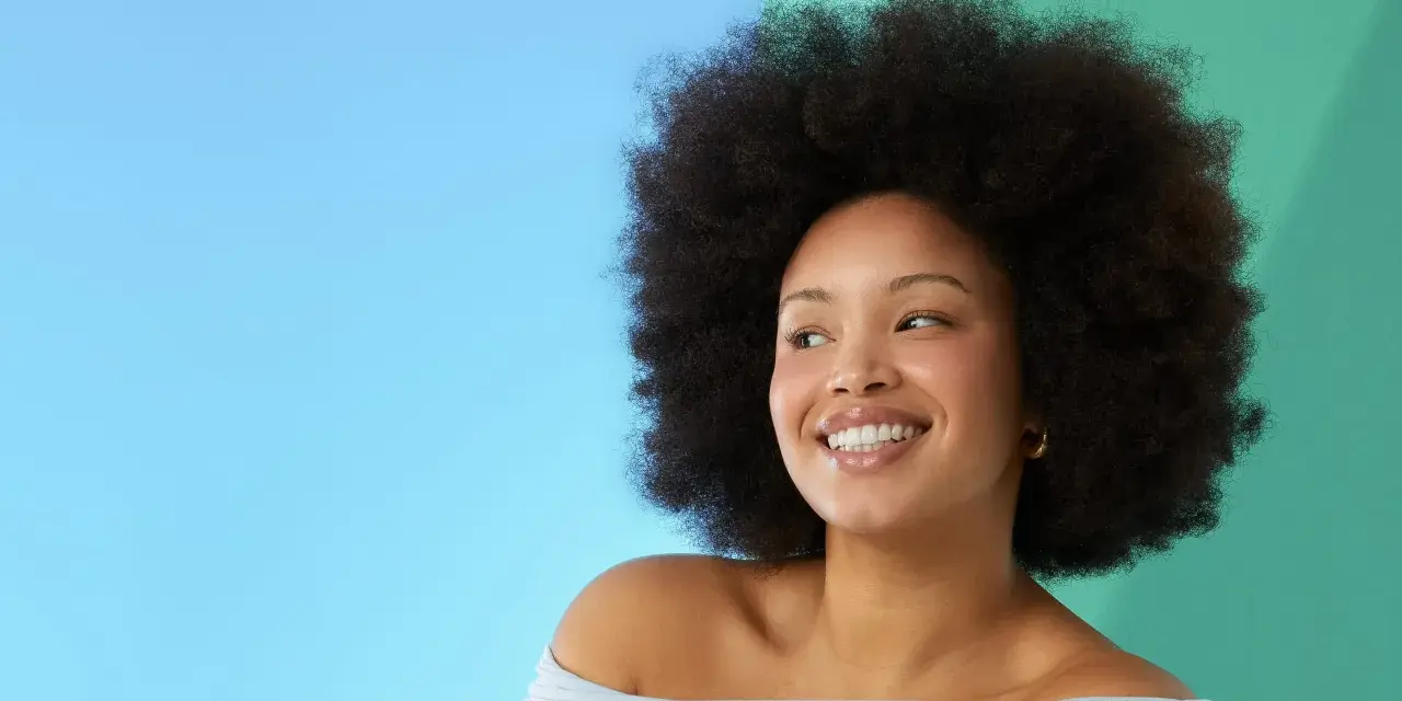 Lächelnde Frau mit Afro-Frisur vor blau-grünem Hintergrund.