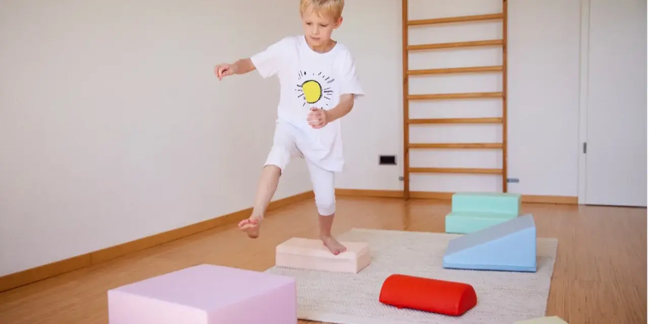 Junge übt Balancieren auf bunten Blöcken. Ergotherapie fördert die Frustrationstoleranz bei Kindern.