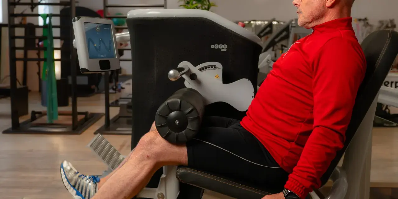 Mann trainiert Beine an einem Gerät, unterstützt von **private Physiotherapeuten** für optimale Ergebnisse.