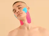 Mann mit geschlossenen Augen, dessen Kiefergelenk und Hals mit pinken und blauen Kinesio-Tapes versorgt sind.