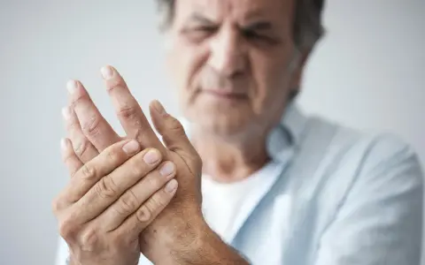 Mann hält seine Hand, da seine Finger schmerzen beim Beugen.
