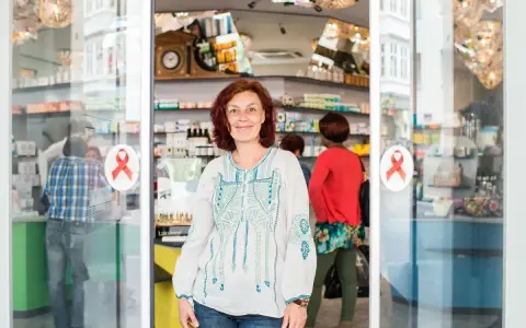 Frau lächelt vor einer Apotheke mit roten Aids-Schleifen am Eingang.