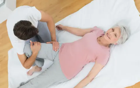 Physiotherapeut unterstützt ältere Frau bei Übungen für den Beckenboden. Sie lächelt zufrieden.