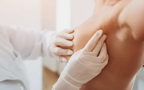 Arzt in Handschuhen tastet Brust ab.