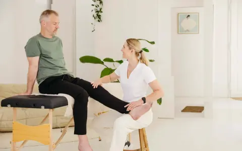 Physiotherapeutin hilft Mann mit Ischias-Schmerzen bei Dehnübungen. Sie streckt sein Bein, um die Nerven zu entlasten.