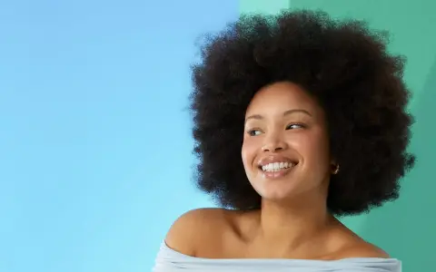 Lächelnde Frau mit Afro-Frisur vor blau-grünem Hintergrund.