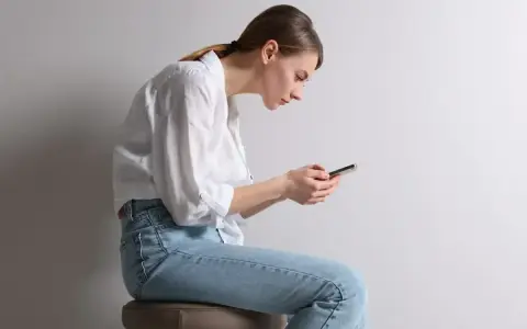 Frau mit gebeugtem Rücken und Handy. Schlechte Haltung kann zu einem Buckel im Nacken Ursache sein.