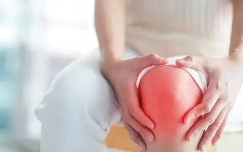 Hände umfassen ein schmerzendes Knie, das rot aufleuchtet, ein Zeichen für Arthrose im Knie.