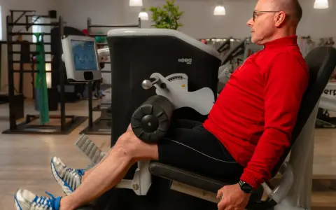 Mann trainiert Beine an einem Gerät, unterstützt von **private Physiotherapeuten** für optimale Ergebnisse.