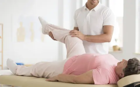 Ein Physiotherapeut unterstützt eine ältere Frau bei einer Beinübung im Rahmen einer PNF Therapie.
