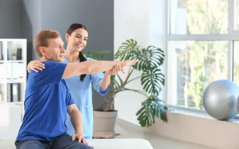 Ein Physiotherapeut unterstützt einen Patienten bei der Armbewegung.