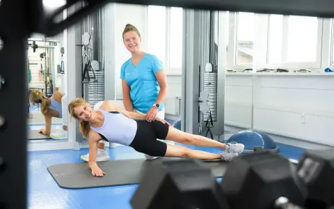 Physio-Übung: Frau macht Seitenstütz, Therapeutin hilft.