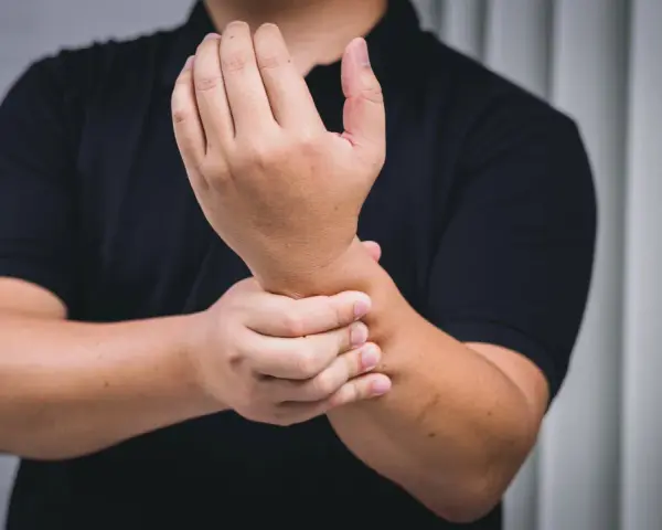 Mann hält schmerzend Handgelenk, deutet auf chronische Tendinopathie.