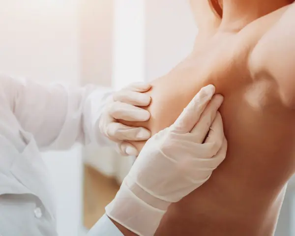 Arzt in Handschuhen tastet Brust ab.