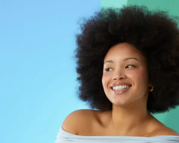 Lächelnde Frau mit Afro-Frisur vor blau-grünem Hintergrund.