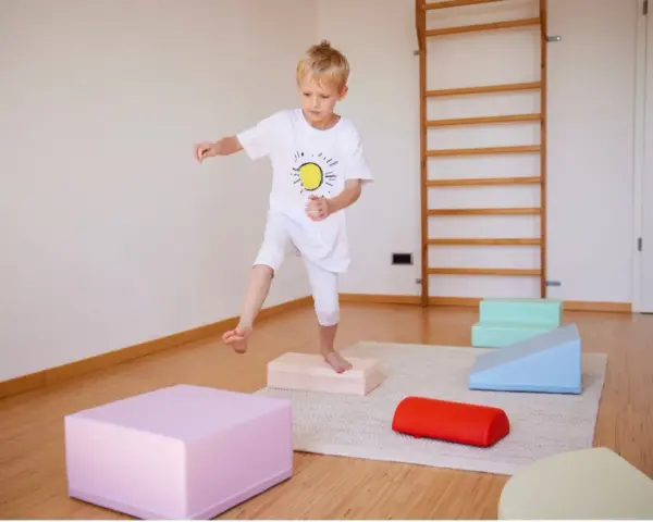 Junge übt Balancieren auf bunten Blöcken. Ergotherapie fördert die Frustrationstoleranz bei Kindern.
