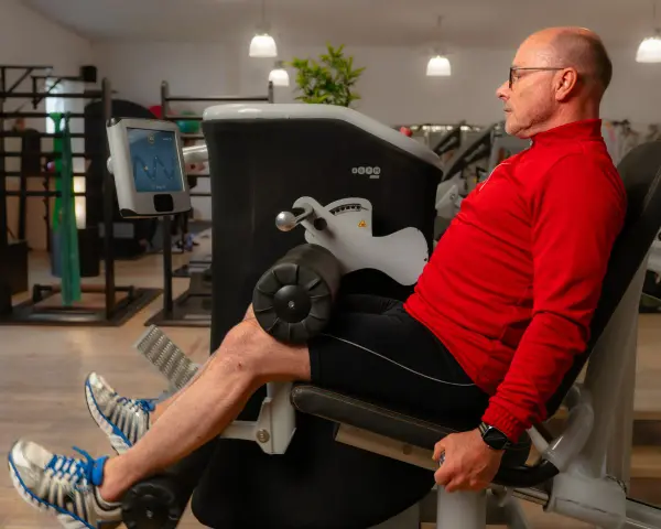 Mann trainiert Beine an einem Gerät, unterstützt von **private Physiotherapeuten** für optimale Ergebnisse.
