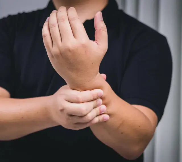 Mann hält schmerzend Handgelenk, deutet auf chronische Tendinopathie.