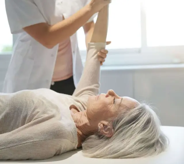 Physiotherapeutin unterstützt ältere Frau bei der Armbewegung. Dies ist Teil einer mld behandlung zur Verbesserung der Beweglichkeit.