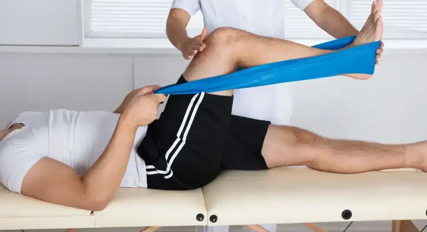 Therapeut dehnt Bein mit blauem Band zur Behandlung von Plica-Syndrom, inspiriert von Liebscher & Bracht Methoden.
