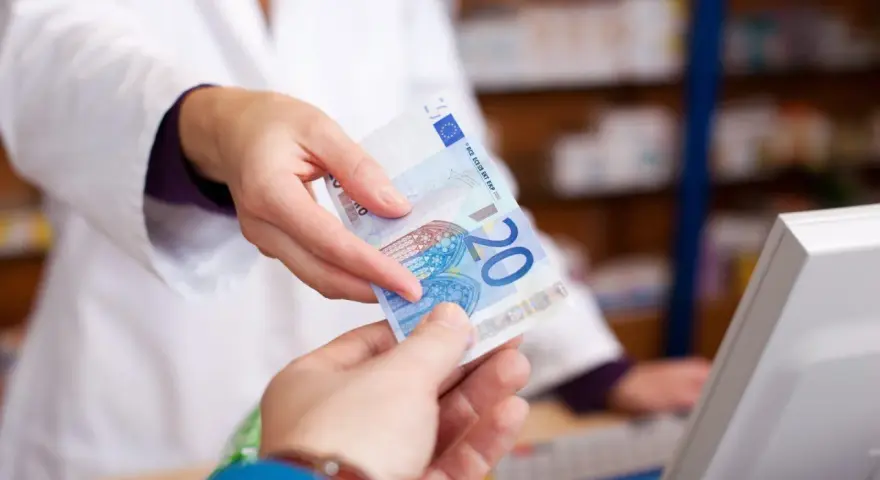 Eine Person in einem weißen Kittel reicht einen 20-Euro-Schein. Möglicherweise zur Bezahlung von Krankengymnastik Kosten.
