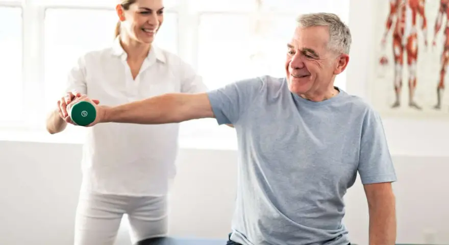 Mann hebt Hantel unter Anleitung einer Therapeutin. Physiotherapie nach Bobath hilft bei der Rehabilitation.