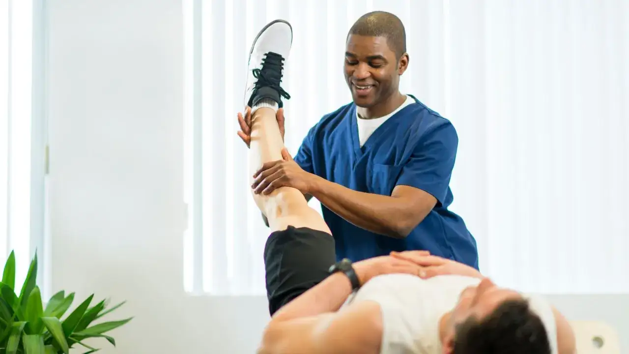 Physiotherapeut dehnt das Bein eines Patienten. Die Frage 