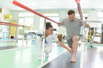 Mann übt nach Physiotherapie unter Anleitung einer Therapeutin auf einer Matte.