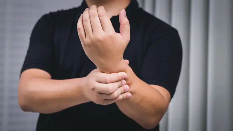 Mann hält schmerzend Handgelenk, deutet auf chronische Tendinopathie.