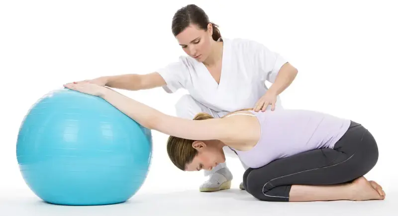 Therapeutin unterstützt Frau bei Bobath-Therapie für Erwachsene mit Gymnastikball.