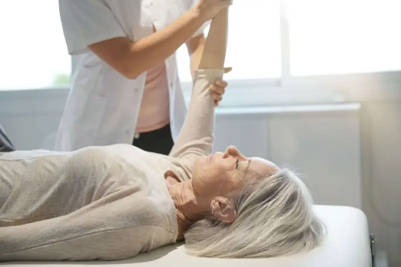 Physiotherapeutin unterstützt ältere Frau bei der Armbewegung. Dies ist Teil einer mld behandlung zur Verbesserung der Beweglichkeit.